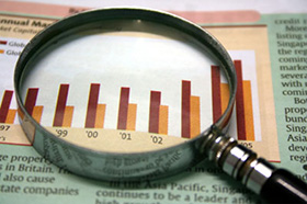 A magnifying glass focusing on a graph in the business section of the newspaper.
